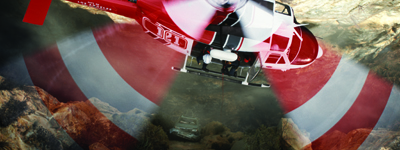 A red helicopter flies over a rugged, rocky canyon landscape.