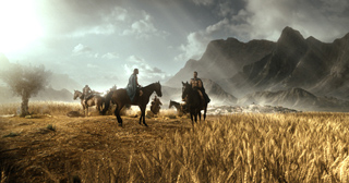 People riding horses through a vast golden wheat field toward rugged mountains under a bright, cloudy sky.