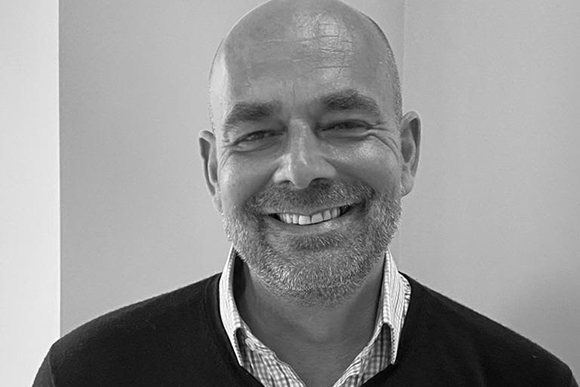 Black and white headshot of a smiling, bald man with a salt-and-pepper beard wearing a collared shirt.