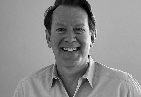 Black and white headshot of a middle-aged man smiling against a plain background.