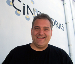 A smiling man in a black t-shirt stands in front of a white Cinemark banner.