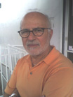 A man with glasses and a white beard wearing an orange polo shirt.