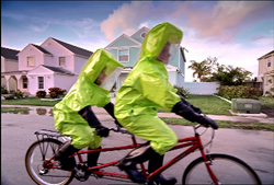Two people in lime green protective suits riding a red tandem bicycle on a suburban street.