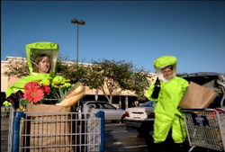 Two people in neon green hazmat suits with face shields stand next to shopping carts in a parking lot.