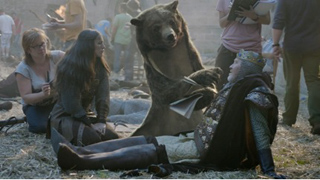 A person in a bear costume holds a script while interacting with an actor dressed as a king on a film set.
