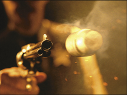 A close-up of a bullet flying through smoke after being fired from a revolver.