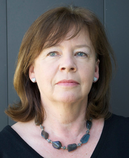 A woman with shoulder-length brown hair, blue eyes, and a stone necklace looking forward.