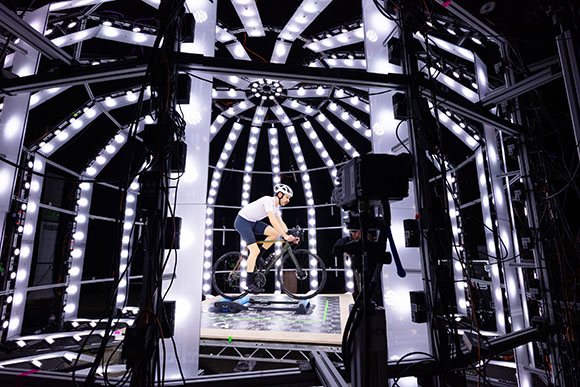 A person on a bicycle riding on a platform inside a dome-shaped structure lined with bright LED lights.