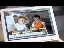 A white laptop screen shows a video of two infants sitting in high chairs indoors.
