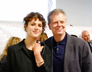 A woman with curly hair and a man in a dark blazer smiling for a photo.