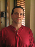 A man with dark hair wearing a red button-up shirt looking forward.