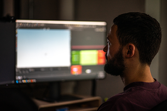 Side profile of a man with a beard looking at a bright computer screen in a dark room.