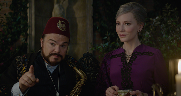 A man wearing a red fez points his finger while a woman in a purple dress looks on.