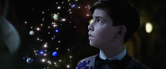 A young boy gazes upward at glowing planets and sparkling stars in a dark space.