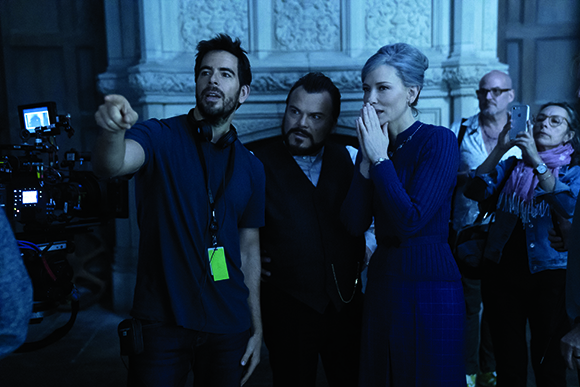 A man in a blue shirt points off-camera while a woman in a blue dress looks on with a hand to her mouth.