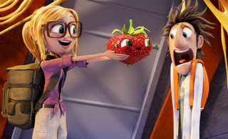 A blonde girl in glasses holds out a smiling strawberry toward a man with a shocked expression.