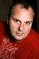 A man with short dark hair wearing a red graphic t-shirt looking directly at the camera.