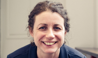 A smiling woman with dark, wavy hair pulled back, looking directly at the camera.