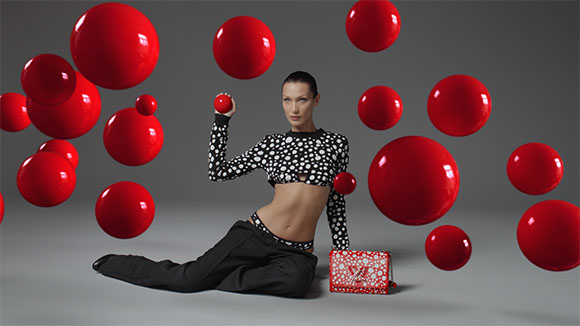 A model in a polka dot crop top sits on the floor surrounded by various sized floating red spheres.