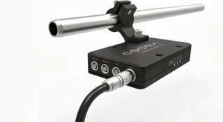 A black electronic module with various ports and a connected cable, holding a long metal rod in a clamp.