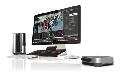 Computer monitor displaying video editing software, a control surface, keyboard, mouse, and external hardware.