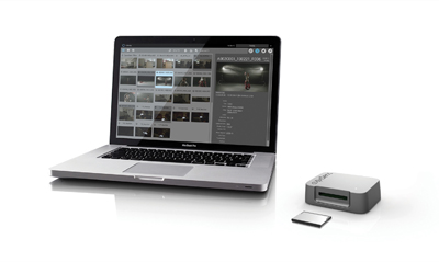 A silver laptop displaying a media library next to a small external hard drive and a memory card.