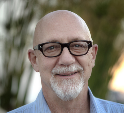 A bald man with black-rimmed glasses and a white goatee smiling at the camera.