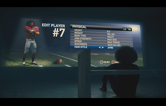 A person sits in silhouette before a large screen showing a football player's physical attribute settings.