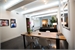 A bright, modern room featuring a large wooden table in the foreground and a living area in the background.