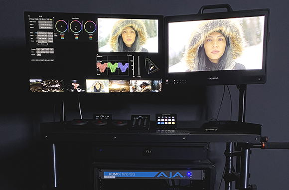 Dual monitors displaying video editing software and a close-up of a person in a fur-lined hood.
