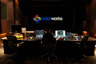 A person sits at a professional video editing desk facing a large screen displaying the Colorworks logo.