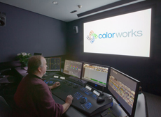 A man sits at a desk with four computer monitors in a dark studio with a large screen displaying a logo.