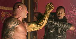 A shirtless man with a golden arm faces a man in dark armor in a red room.
