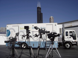 Three professional video cameras on tripods positioned in front of a white Columbia College Chicago truck.
