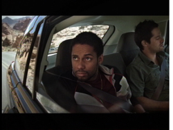 Two men sit in the back seat of a moving vehicle looking out the windows.