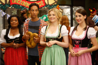 Four people in traditional German dirndls and lederhosen stand together at an Oktoberfest event.