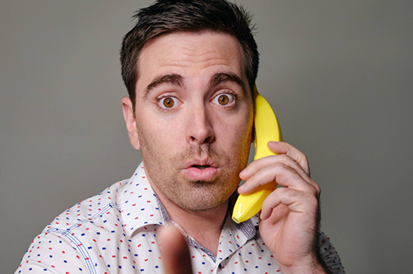 A man with a surprised expression holds a yellow banana to his ear as if making a phone call.