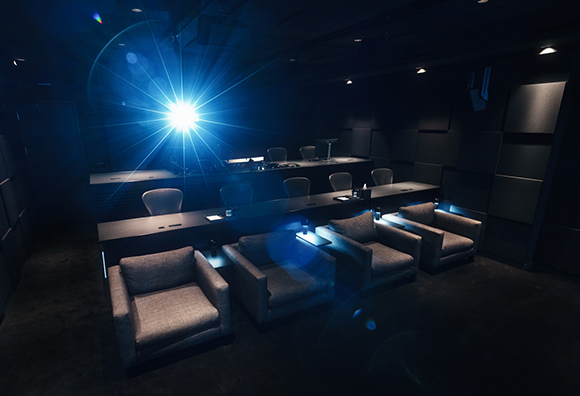 A dark room with grey armchairs, long tables, and a bright blue light flare in the center.