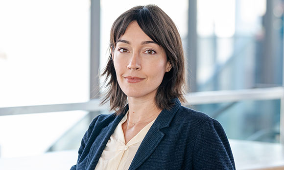 A woman with shoulder-length dark hair wearing a dark blue blazer and a cream blouse.