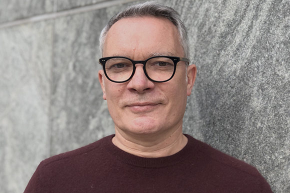 A man with short graying hair and black-rimmed glasses wearing a maroon sweater.