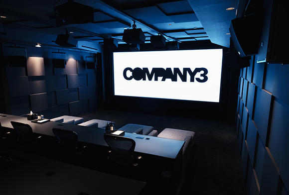 A dark screening room with blue lighting, a large projection screen, and rows of seating.