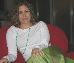 A woman with curly hair wearing a white shirt and green beaded necklace sits on a red couch.