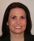 A smiling woman with long dark hair and a black blazer against a neutral background.