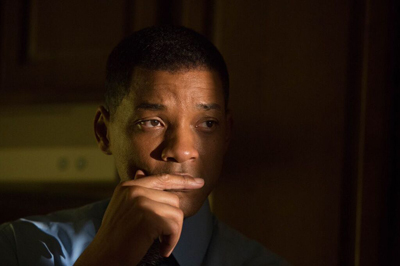 A man in a blue shirt looks off-camera with a contemplative expression, resting his chin on his hand.