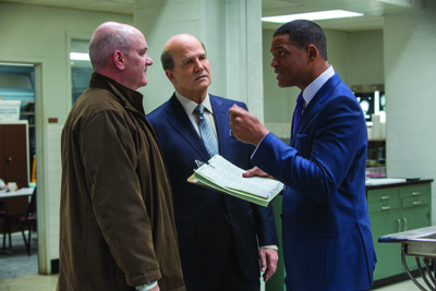 A man in a blue suit gestures while talking to two other men in an office.