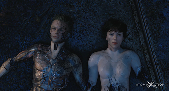 A male cyborg and a female humanoid lie side-by-side on a dark, rocky ground.