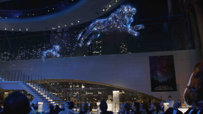 Two glowing blue lion figures made of light particles leap through the air above a nighttime gathering.