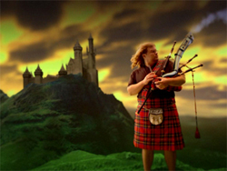 A man in a red plaid kilt plays bagpipes against a backdrop of a castle on a hill at sunset.