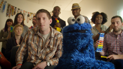 A group of diverse people smiling and posing behind a large Cookie Monster puppet.
