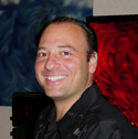A smiling man with short dark hair wearing a black button-down shirt.
